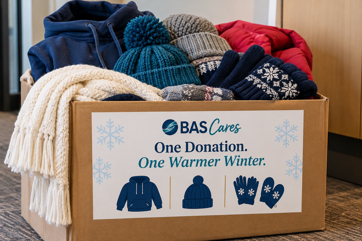 BAS Cares collection box filled with hoodies, knit hats, a scarf, gloves, and mittens, labeled One Donation. One Warmer Winter.