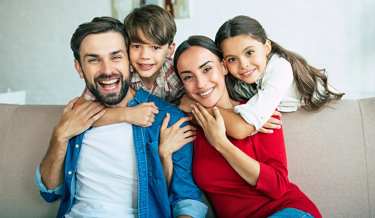 Smiling parents with their two children at home, representing this week's question about using a Dependent Care FSA for babysitting expenses