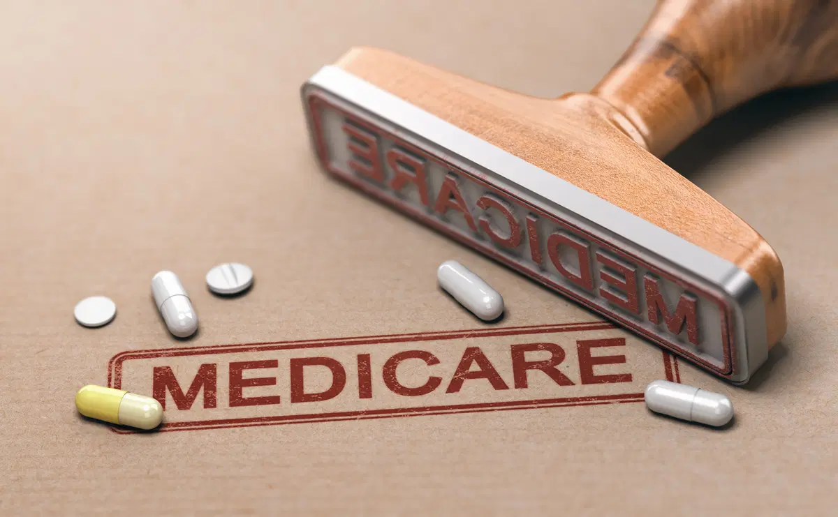 Wooden rubber stamp beside a red MEDICARE stamp imprint on brown paper, surrounded by scattered pills and capsules