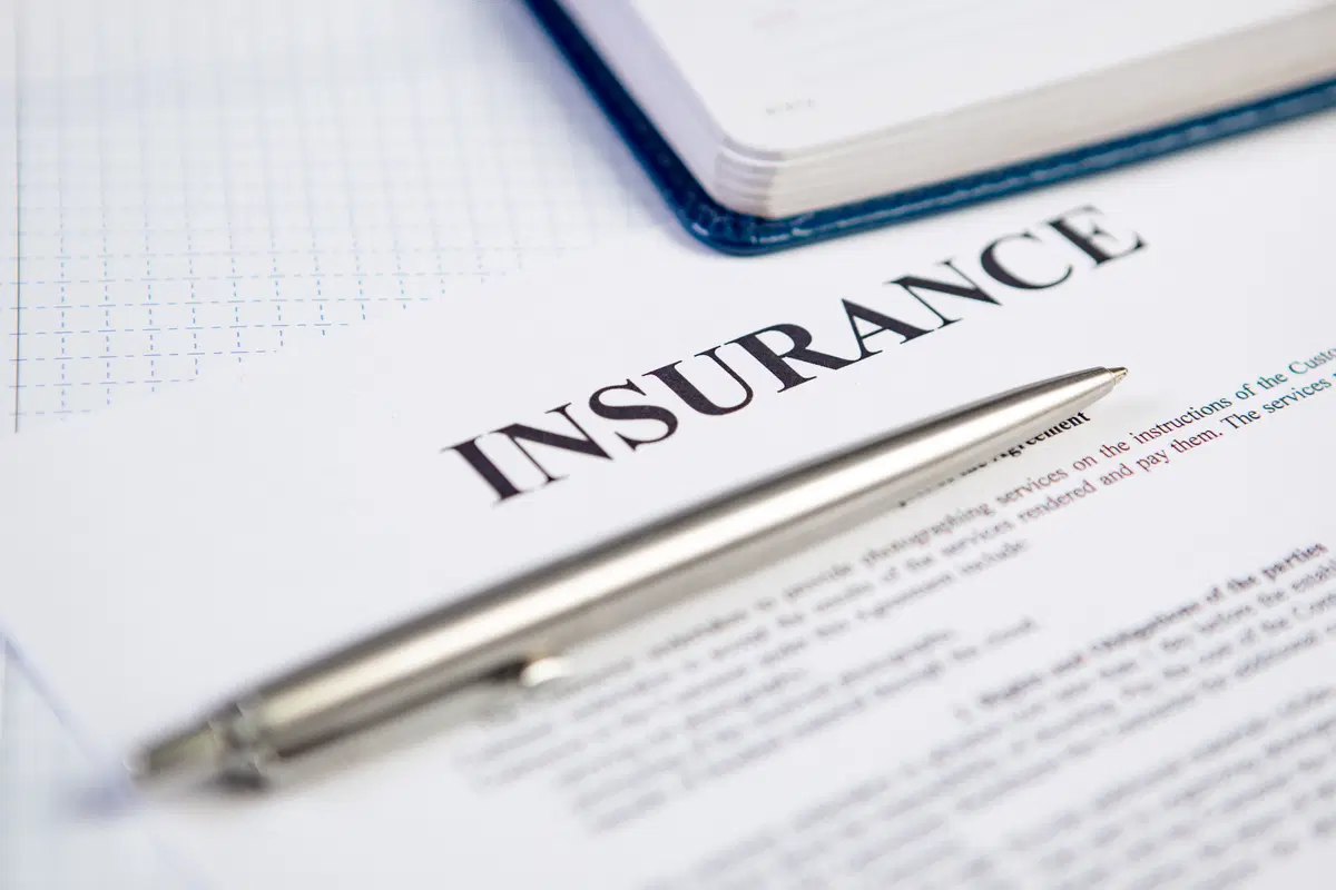 Silver pen resting on a document titled Insurance beside an open notebook on a desk
